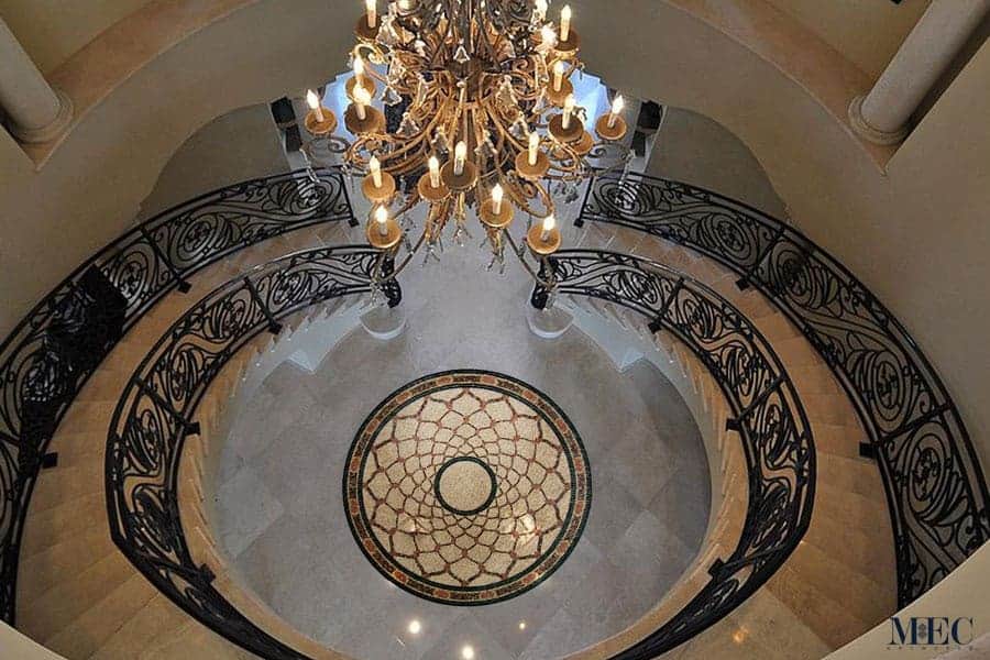 The Armida Mosaic Tile Rug is a stunning centerpiece of this luxurious interior, reflecting the elegance of the chandelier and the intricacy of the railing.