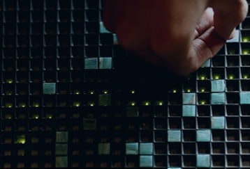 Hand adjusting dark mosaic tile wall, creating a modern, textured interior design.