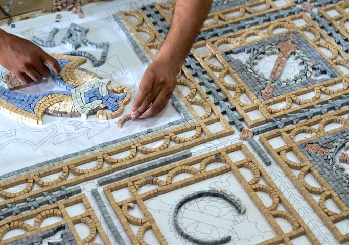 A detailed view of a mosaicist's hands arranging colorful tiles to form a mosaic design