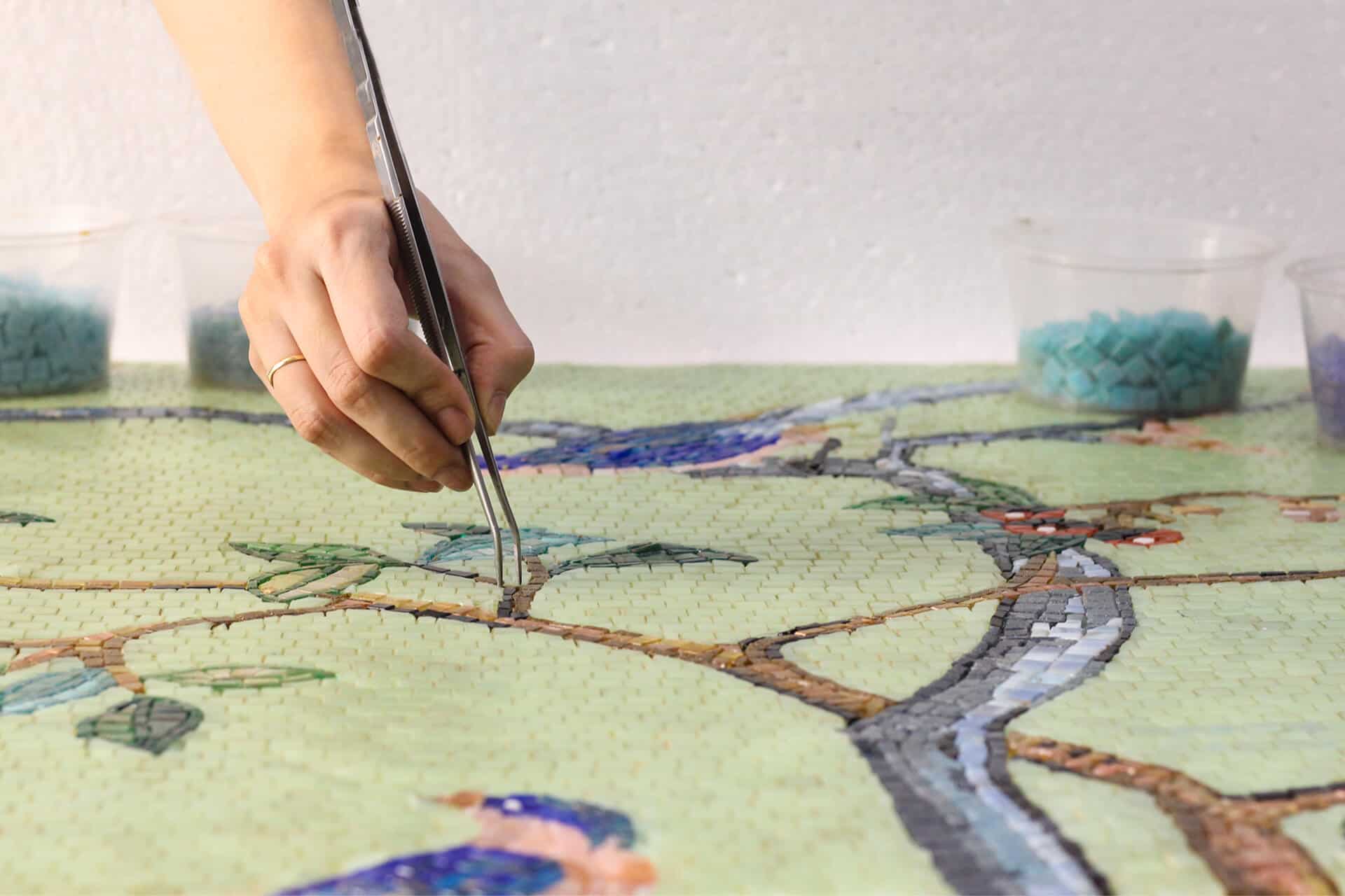 A mosacist hand placing marble mosaic tiles on a colorful mosaic mural.