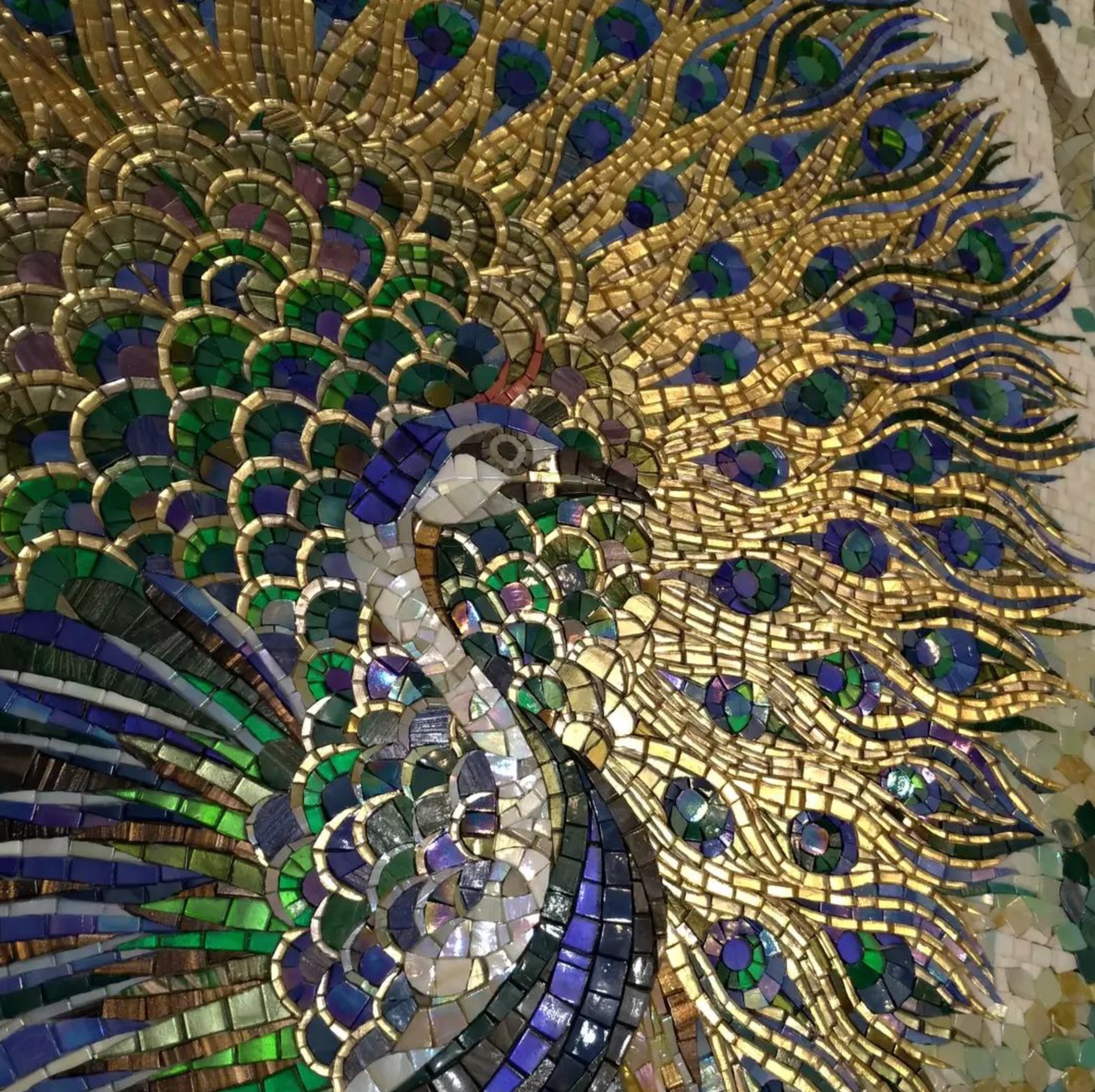
A colorful mosaic artwork depicting a detailed and vibrant peacock with its feathers fanned out, made from various shades of green, blue, gold, and purple tiles.