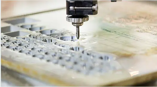 Close-up of a waterjet cutter precisely cutting intricate shapes into a light-colored material.