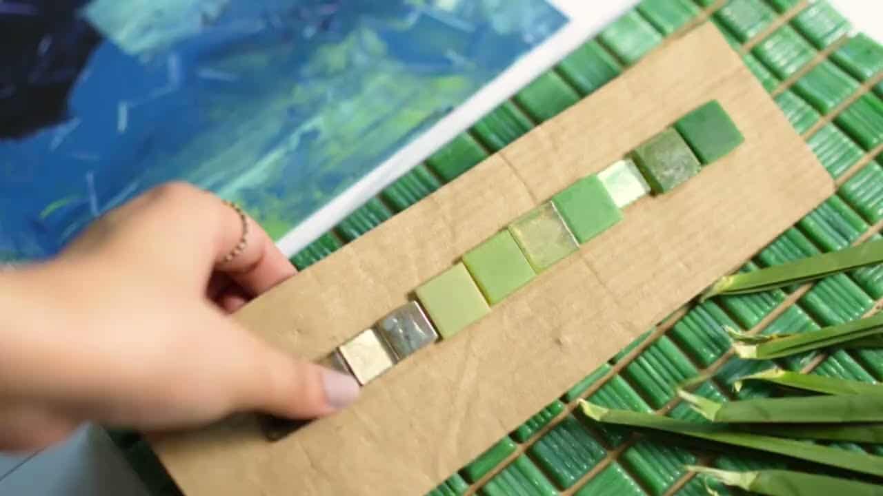 Arranging green mosaic tiles on cardboard for color matching, part of bespoke mosaic design planning process.