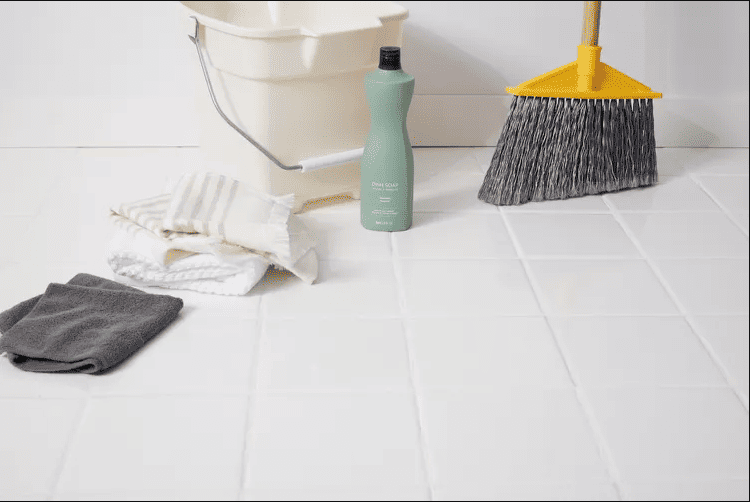 A close-up view of cleaning a  floor with a mop and a bucket of soapy water. The floor has a white geometric pattern.