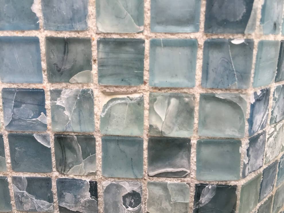 A close up view of a pool waterline glass mosaic tiles with cracks 