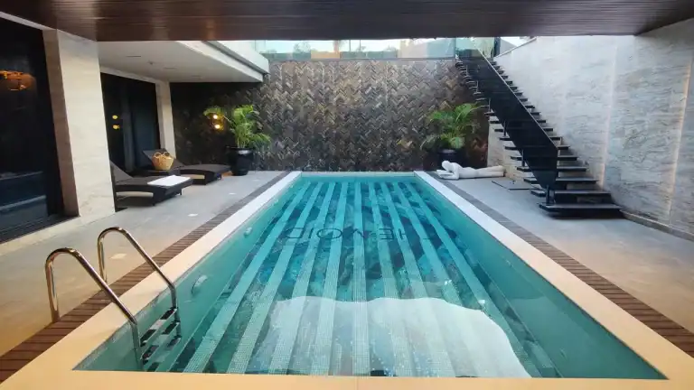 Indoor swimming pool with striped mosaic tile flooring, surrounded by modern decor and black staircase.