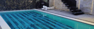 Modern outdoor pool with striped mosaic tiles, black staircase, and a minimalist reclining sculpture nearby.