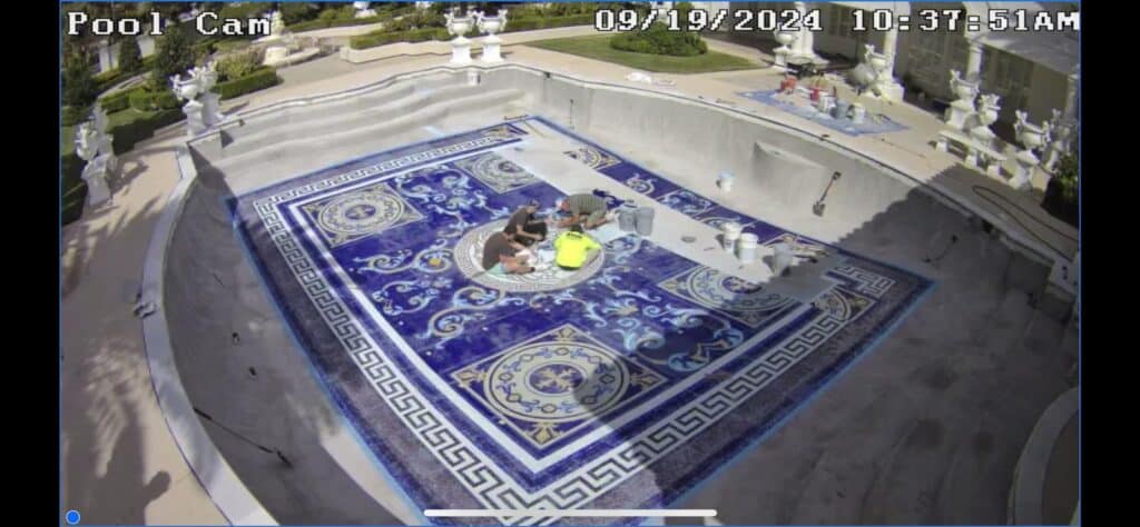 Workers installing intricate blue mosaic artwork with Medusa design at the bottom of an empty luxury pool.