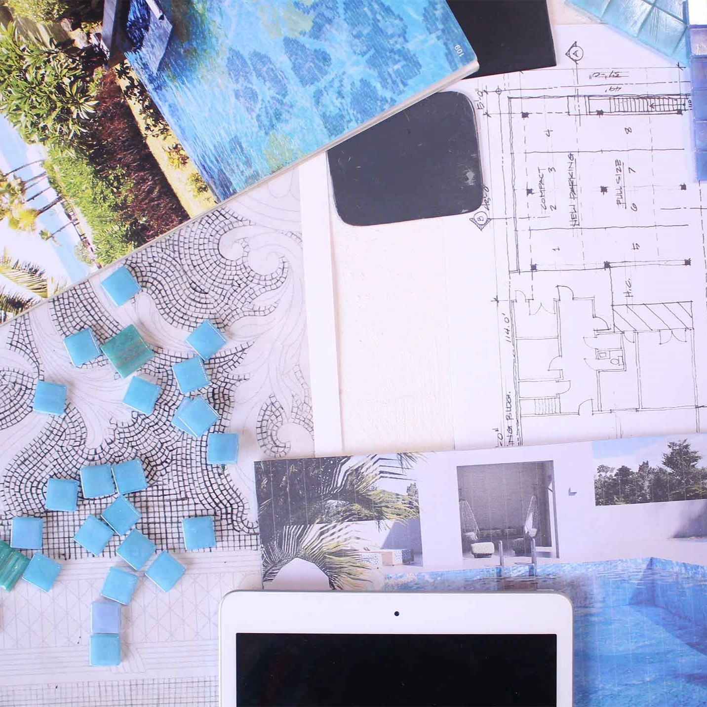 Architectural workspace with blue tile samples, design sketches, floor plans, pool photos, and a tablet.
