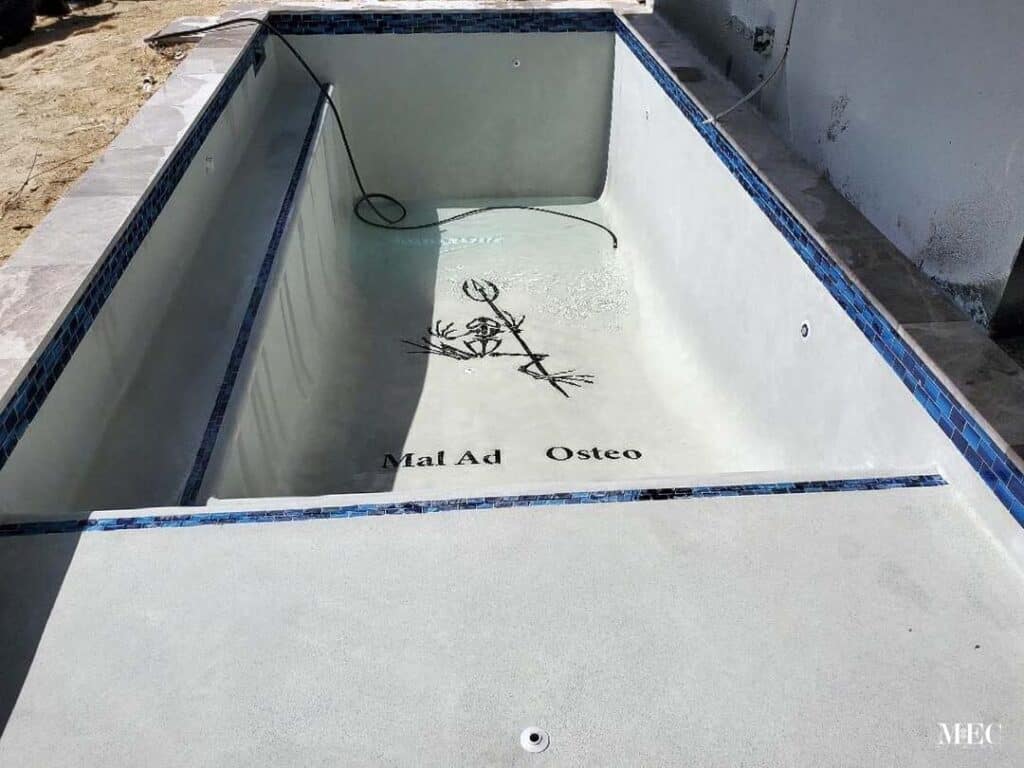 Empty pool featuring skeleton mosaic with text “Mal Ad Osteo,” crafted by MEC Artworks.