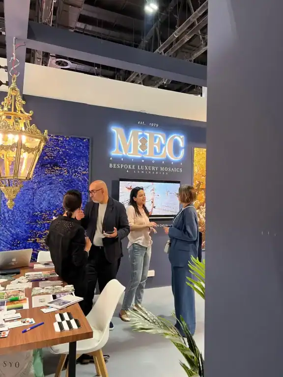 People networking at MEC mosaic booth with blue and gold wall art and chandelier overhead.