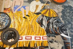 Intricate mosaic art of elephant with riders, surrounded by sorting bowls of colored tile pieces.