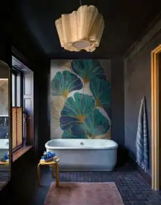 Dark luxury bathroom with ginkgo leaf mosaic behind freestanding tub and soft pendant ceiling light.