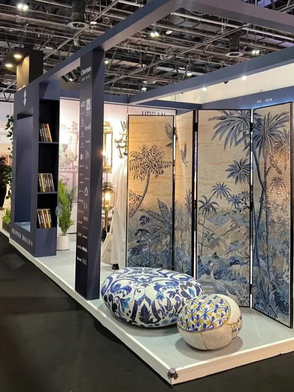 Artistic mosaic exhibition booth with tropical screen panels and patterned ceramic ottomans at interior design fair.