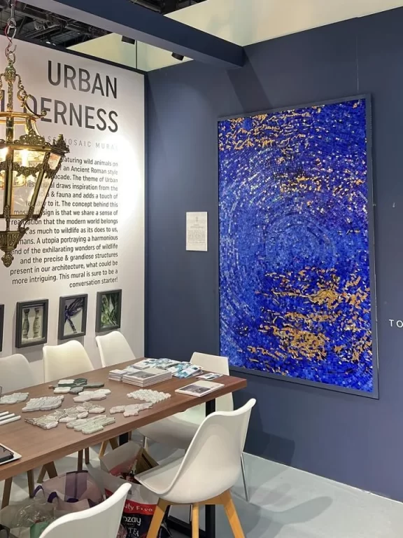 MEC booth with abstract blue mosaic art, chandelier lighting, and mosaic samples on table.