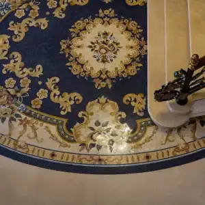 Intricate floral mosaic flooring in navy and gold tones beside elegant staircase with ornate railing.