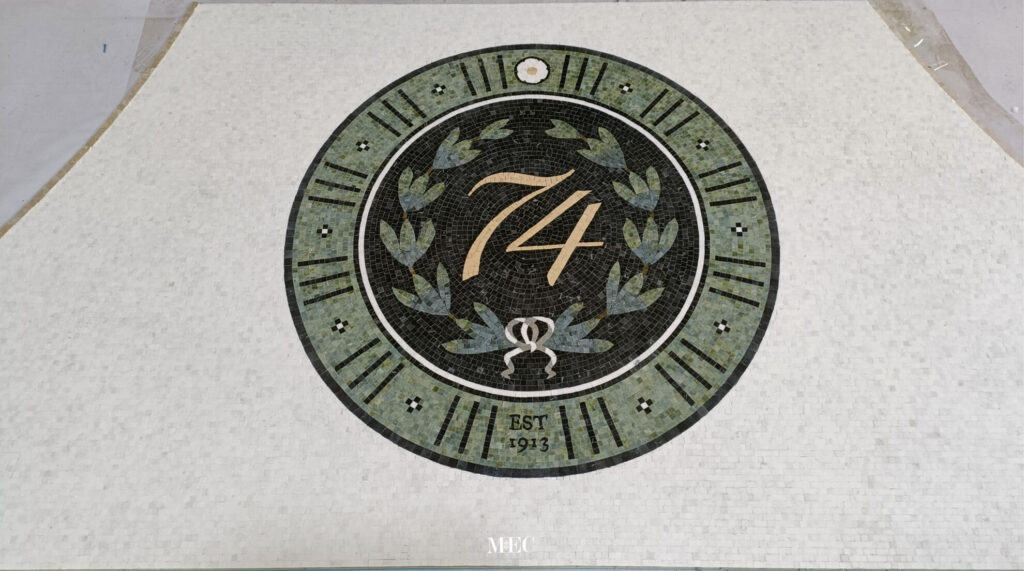 Elegant circular mosaic with laurel wreath and “74” in gold, honoring timeless craftsmanship and tradition.