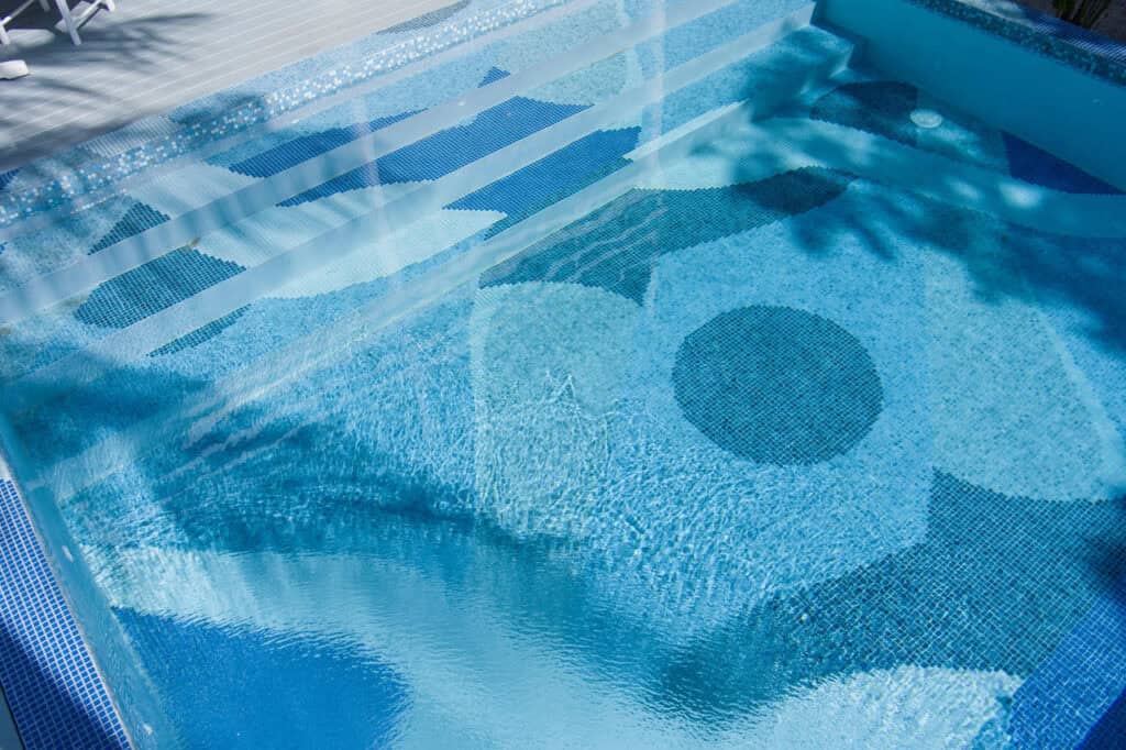 Modern pool with artistic mosaic tile pattern in blue tones, featuring circles, stripes, and wave reflections.