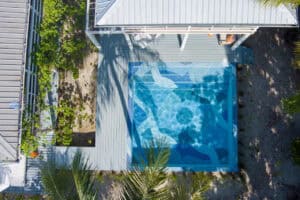 Aerial view of square mosaic-tiled pool with geometric patterns, sunlit reflections, and sleek modern decking.