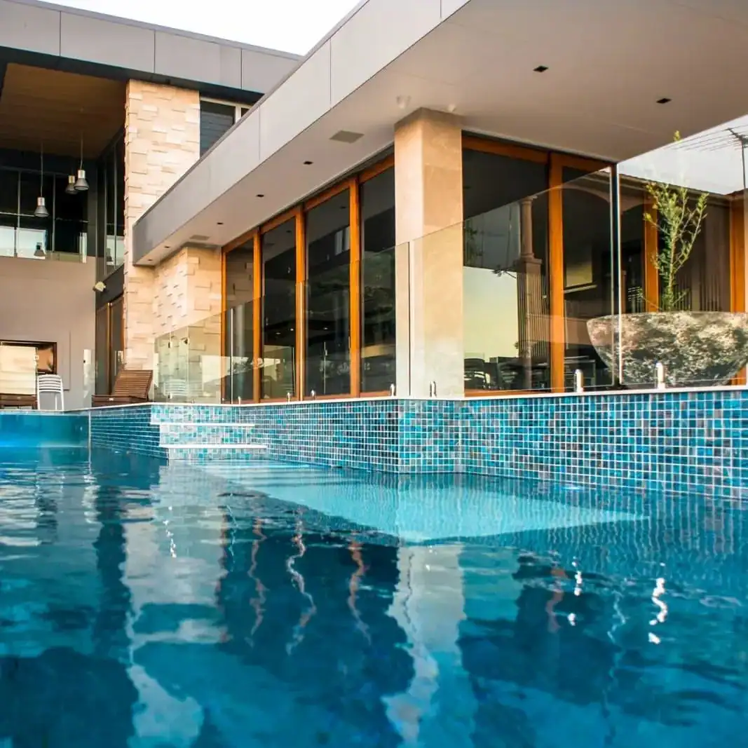 Modern outdoor pool with blue glass mosaic tiles, clean rectangular layout, and reflective water effect against a contemporary villa.
