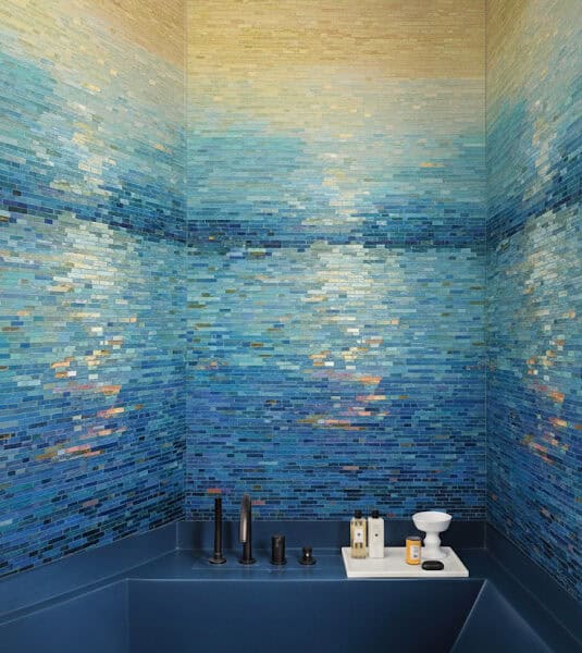 Luxurious shower with gradient glass mosaic tiles transitioning from golden yellow to deep ocean blue, creating a sunset-over-water effect with matte black fixtures.