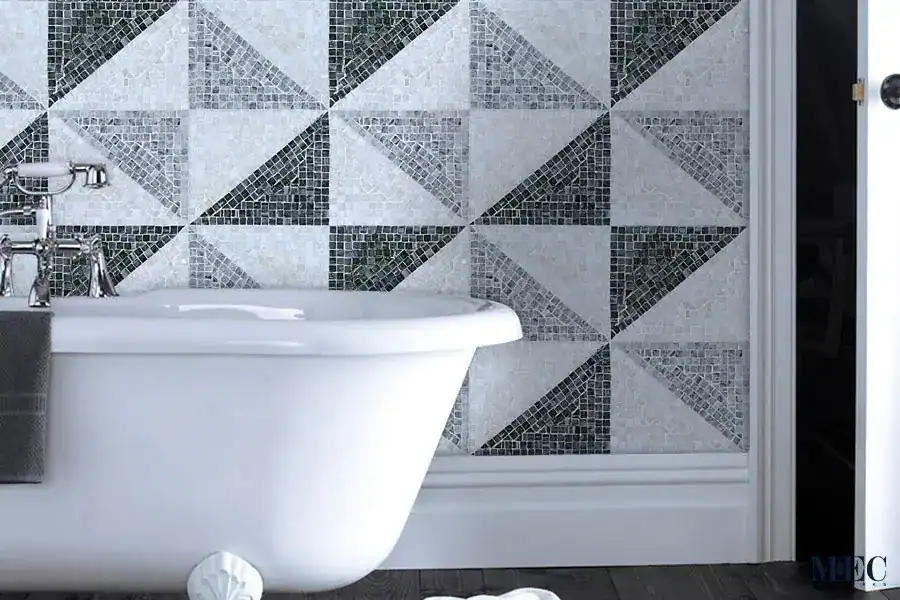 A luxury bathroom with creative geometric mosaic tile ideas with alternating triangles and squares in shades of grey and white marble behind a classic white bathtub.