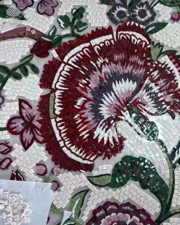 Close-up of a handcrafted mosaic featuring a large maroon, pink, and white Ottoman Iznik carnation pattern with green stems on a white tiled background.