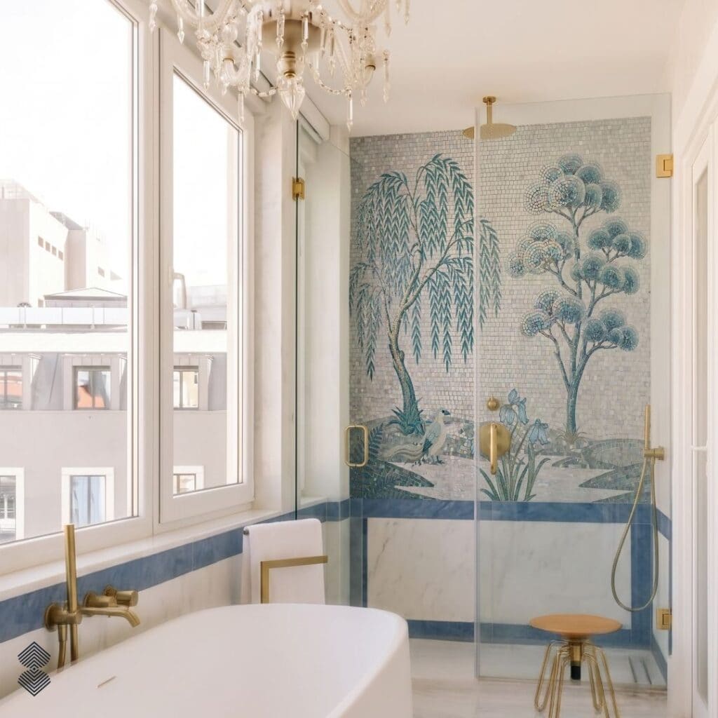 A bright bathroom with a white freestanding tub and a glass shower showcasing a teal and blue mosaic wall with a prominent willow tree, blue iris flowers, and a resting heron.