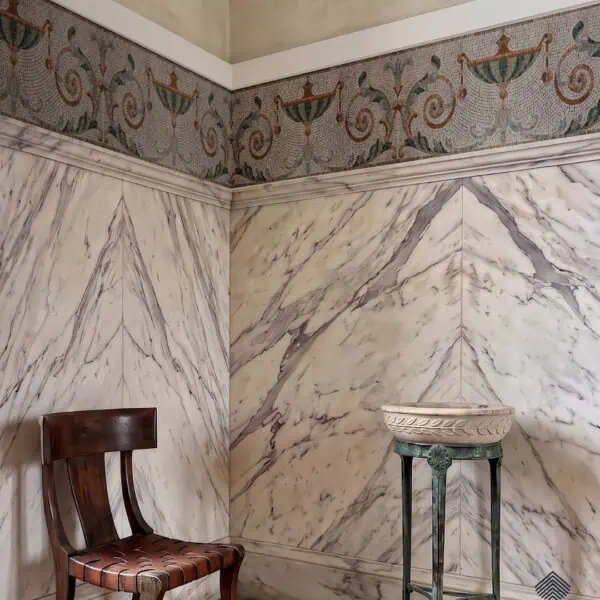 A classical Roman border mosaic frieze of urns and acanthus scrolls wrapping a wall corner above marble paneling.