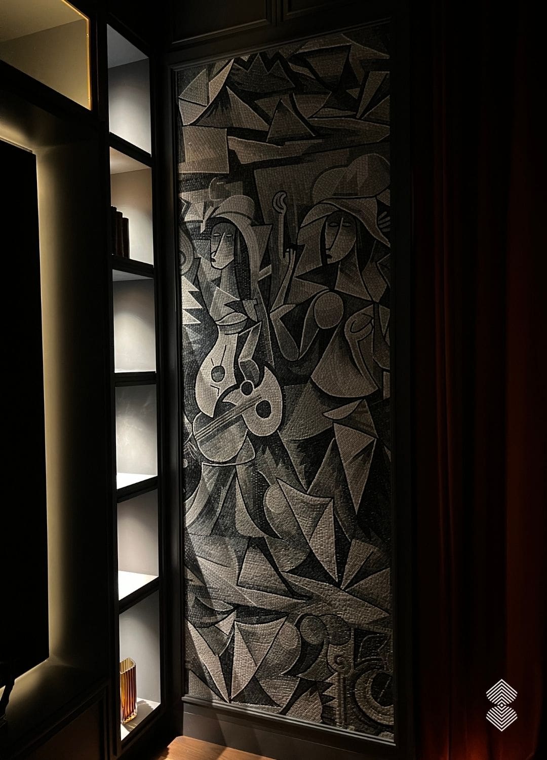 A tall cubist figures wall mosaic showing two musicians in fractured gray and black stone tesserae, installed on a cafe wall.