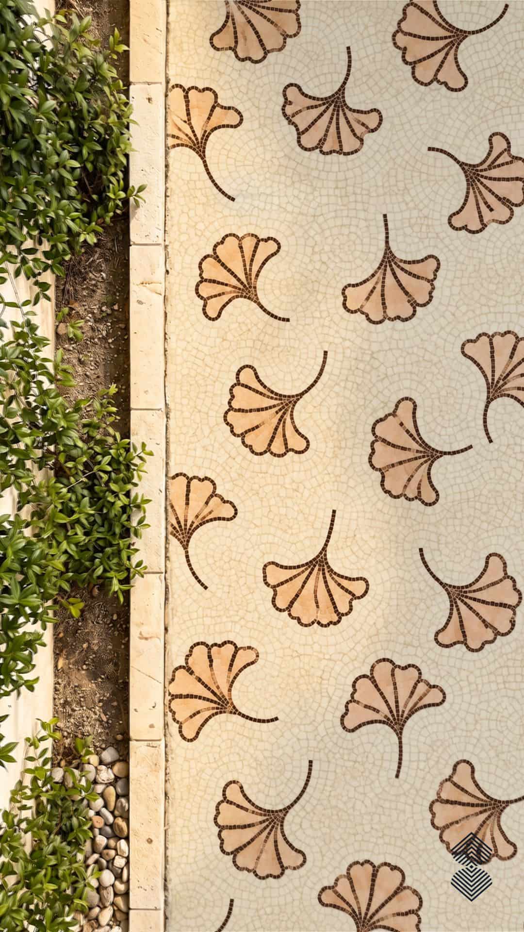 A ginkgo leaf mosaic walkway shows scattered fan-shaped ginkgo leaves in tan and peach stone tesserae set into a cracked cream path beside a planted garden border.