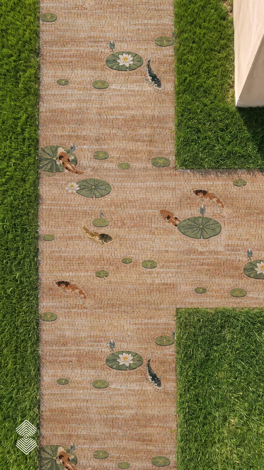 Overhead view of a koi pond walkway mosaic set into a garden path with swimming koi and lily pads flanked by lawn.