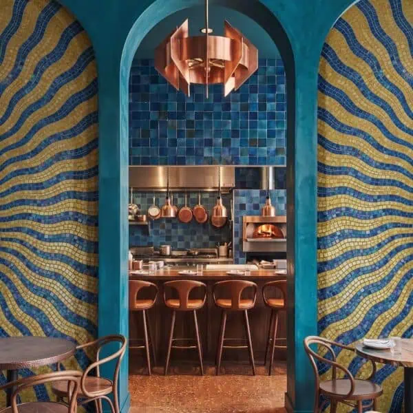 Wavy Gold and Blue Border Mosaic Archway Panels A wavy border mosaic wall panel in gold and blue glass tesserae framing an arched doorway in a restaurant.