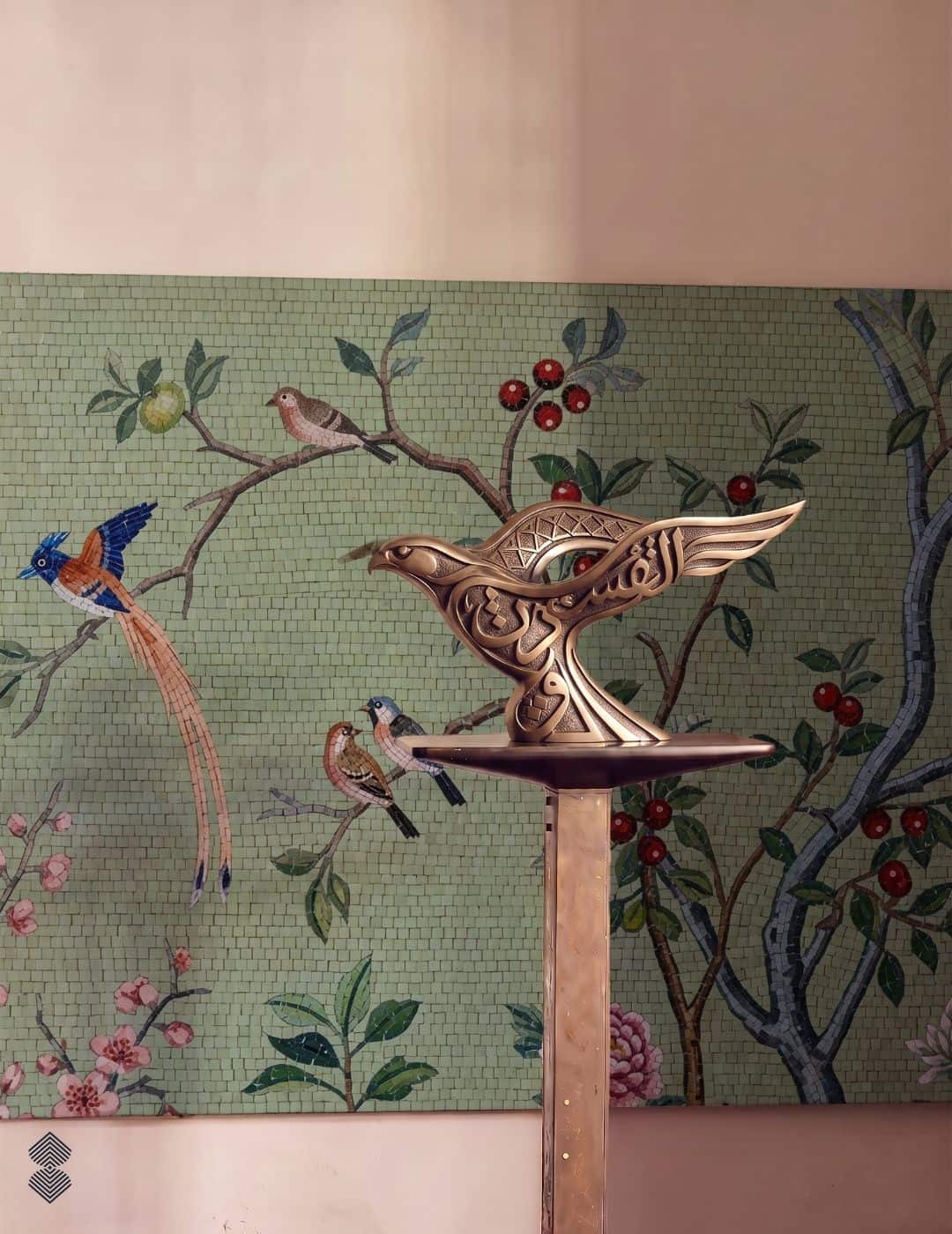 A bird blossom mosaic mural on a sage-green wall showing birds perched on flowering branches with red berries