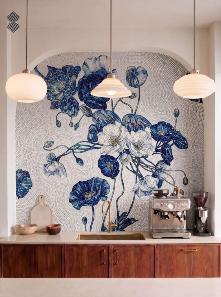 An arched kitchen nook featuring a blue and white mosaic floral wall mural behind a sink and espresso machine with pendant lights overhead.