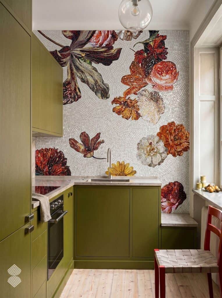 A full-wall mosaic mural displaying large, hand-cut floral blossoms in warm orange, red, and cream tones behind olive green kitchen cabinetry.