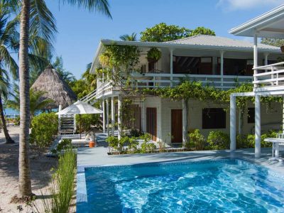 Luxury villa with sparkling mosaic-tiled pool, surrounded by tropical greenery, white railings, and coastal charm.
