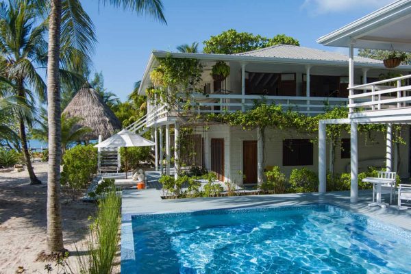 Luxury villa with sparkling mosaic-tiled pool, surrounded by tropical greenery, white railings, and coastal charm.