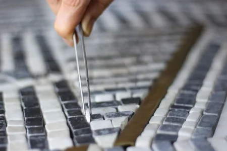 Crafting Your Masterpiece- MEC Artworks Close-up of artisan placing mosaic tile with tweezers, showcasing intricate craftsmanship and design precision.