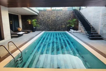 Indoor swimming pool with striped mosaic tile flooring, surrounded by modern decor and black staircase.