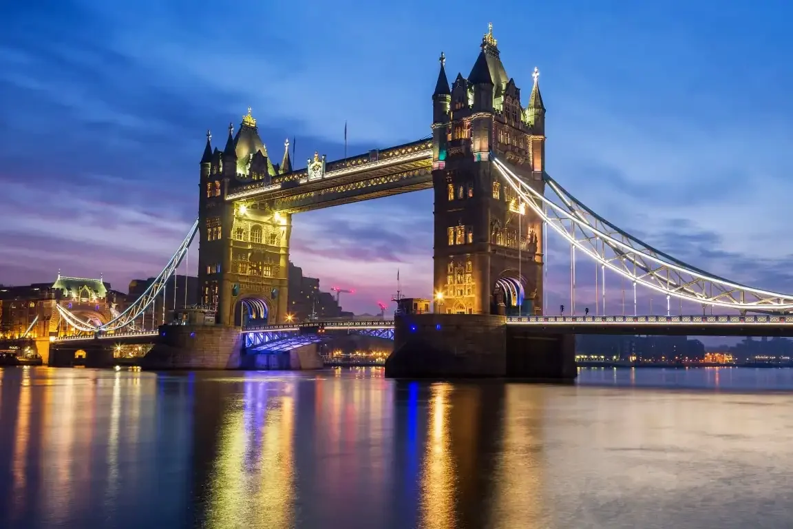 Tower Bridge in London illuminated at twilight, reflecting beautifully on the calm River Thames waters.