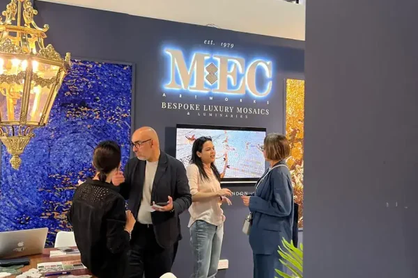 People networking at MEC mosaic booth with blue and gold wall art and chandelier overhead.