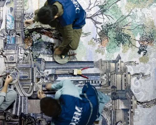 MEC artisans carefully crafting a large architectural mosaic mural with trees using tiny stone tesserae.