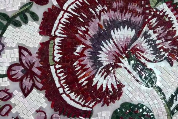 Close-up of a handcrafted mosaic featuring a large maroon, pink, and white Ottoman Iznik carnation pattern with green stems on a white tiled background.