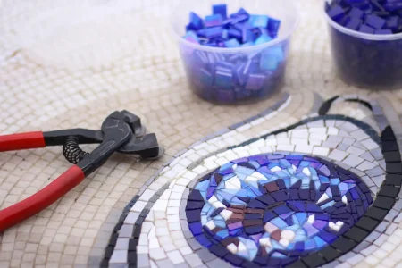 Tailored Design & Proposal- MEC Artworks Mosaic in progress with blue tiles, red pliers, and tools used for precise tile cutting.